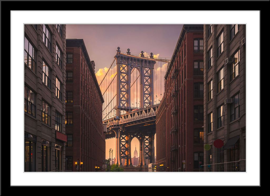 Stadt Architektur Fotografie der Manhattan Bridge durch eine Häuserfront bei Sonnenuntergang in New York. Fotokunst und Bilder online kaufen. Wandbild im Rahmen