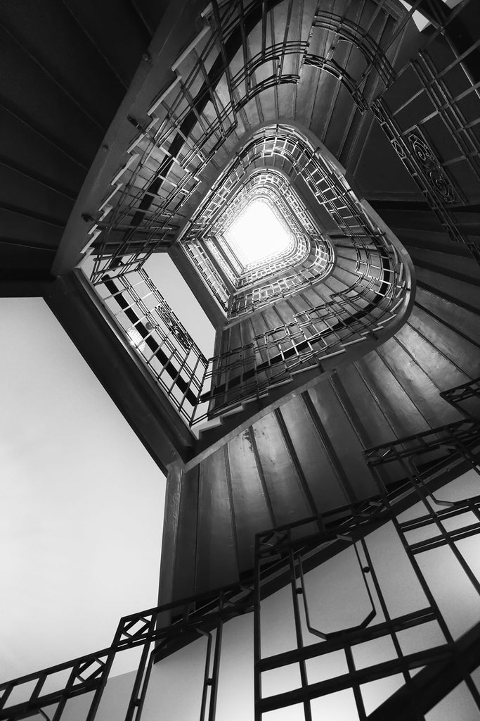Schwarz-Weiß Architektur Fotografie von einem Treppenhaus mit Blick nach oben im Hochformat. Fotokunst und Bilder online kaufen. Wandbild hinter Acrylglas oder als Poster