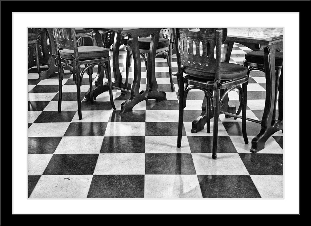 Schwarz-Weiß Fotografie von einem gekachelten Boden mit alten Holz Stühlen. Fotokunst und Bilder online kaufen. Wandbild im Rahmen