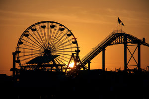 Fotografie einer Silhouette eines Riesenrads und einer Achterbahn bei Sonnenuntergang. Fotokunst und Bilder online kaufen. Wandbild hinter Acrylglas oder als Poster