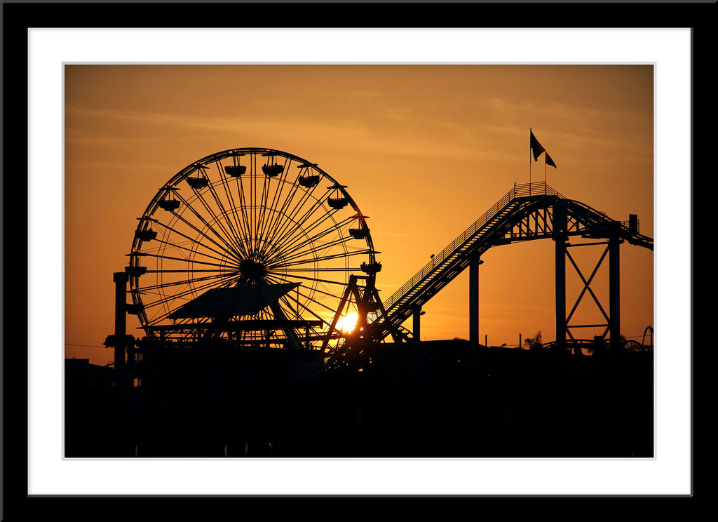 Fotografie einer Silhouette eines Riesenrads und einer Achterbahn bei Sonnenuntergang. Fotokunst und Bilder online kaufen. Wandbild im Rahmen