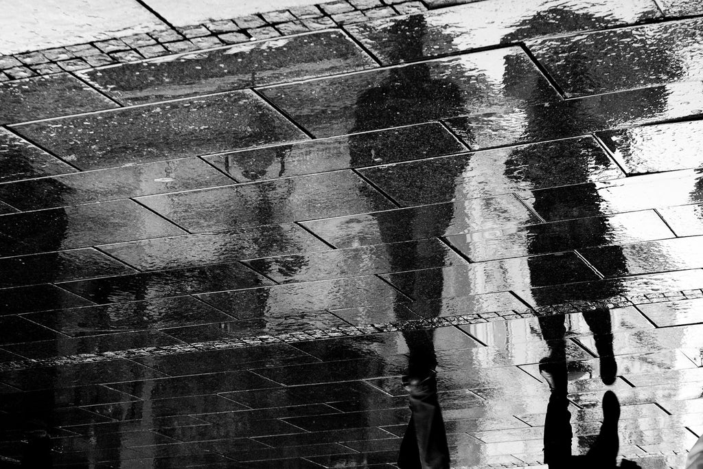Fotografie einer Reflexion von zwei Spaziergängern auf dem Gehsteig. Fotokunst und Bilder online kaufen. Wandbild hinter Acrylglas oder als Poster