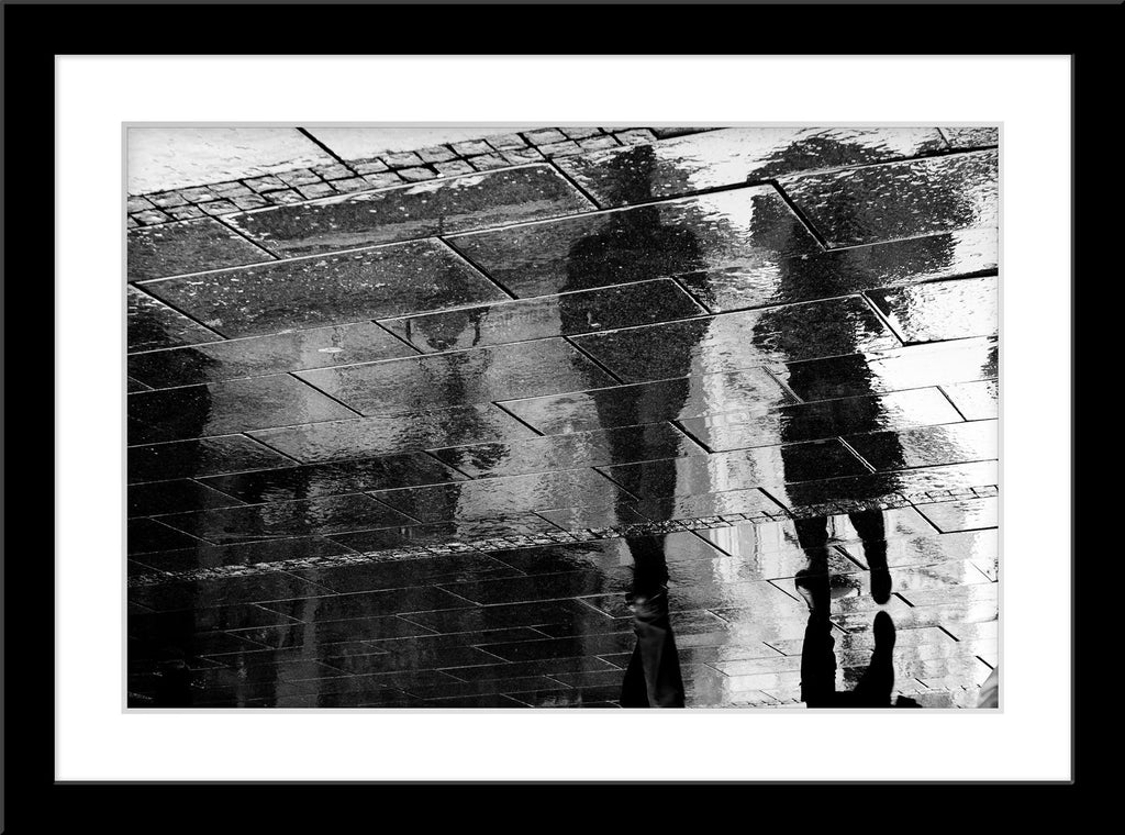 Fotografie einer Reflexion von zwei Spaziergängern auf dem Gehsteig. Fotokunst und Bilder online kaufen. Wandbild im Rahmen