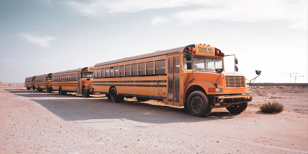 Fotografie von amerikanischen gelben Schulbussen die auf Schotter stehen im Panorama Format. Fotokunst und Bilder online kaufen. Wandbild hinter Acrylglas oder als Poster