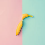 Abstrakte Fotografie von einer in der Mitte geteilten Banane auf rosa und türkisen Hintergrund im quadratischen Format. Fotokunst und Bilder online kaufen. Wandbild hinter Acrylglas oder als Poster 
