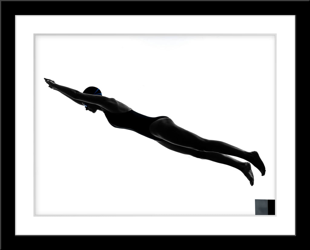 Schwarz-Weiß People Fotografie von einer Schwimmerin die von einem Startblock spring vor weißem Hintergrund. Fotokunst und Bilder online kaufen. Wandbild im Rahmen