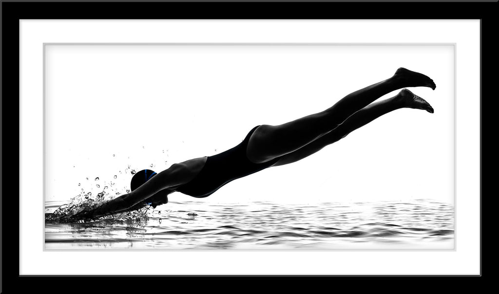 Schwarz-Weiß People Fotografie von einer Schwimmerin die in Wasser eintaucht vor weißem Hintergrund. Fotokunst und Bilder online kaufen. Wandbild im Rahmen