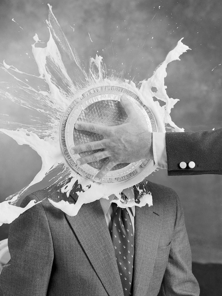 Schwarz-Weiß Fotografie von einem Mann im Anzug der eine Torte ins Gesicht bekommt im Hochformat. Fotokunst und Bilder online kaufen. Wandbild hinter Acrylglas oder als Poster