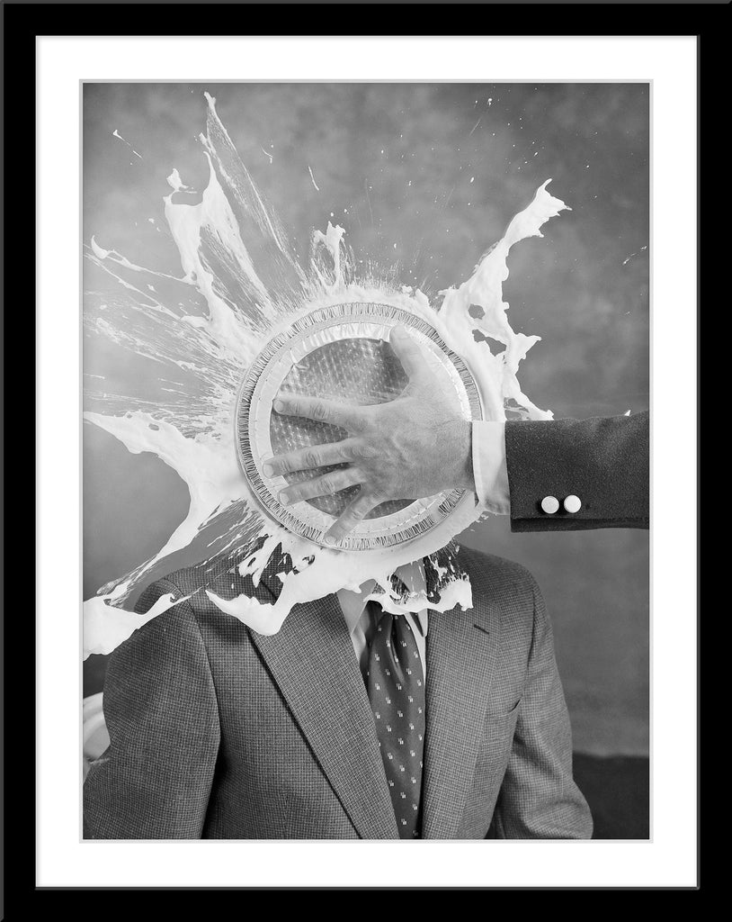 Schwarz-Weiß Fotografie von einem Mann im Anzug der eine Torte ins Gesicht bekommt im Hochformat. Fotokunst und Bilder online kaufen. Wandbild im Rahmen