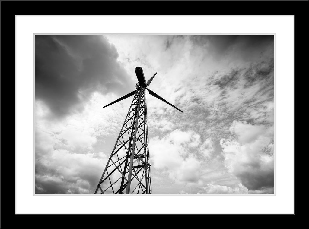 Schwarz-Weiß Fotografie von einem alten Windrad und dramatischem Himmel. Fotokunst und Bilder online kaufen. Wandbild im Rahmen