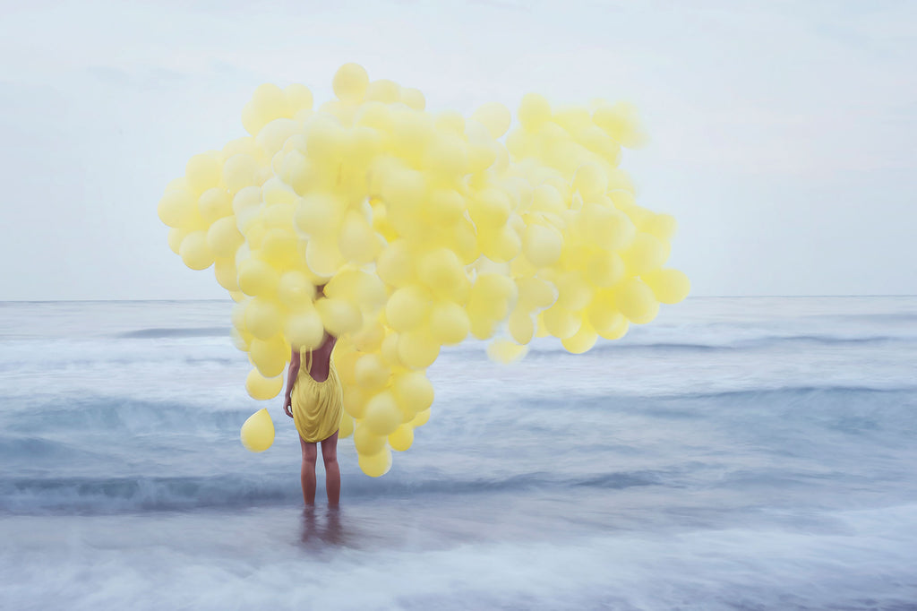 People Fotografie von einer Frau in gelben Kleid mit gelben Luftballons die im Meer steht. Fotokunst und Bilder online kaufen. Wandbild hinter Acrylglas oder als Poster