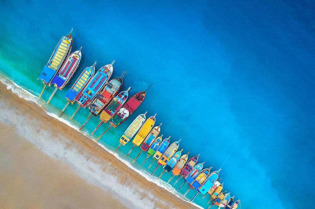 Fotografie von farbigen, nebeneinander liegenden, Fischerbooten am Strand. Fotokunst online kaufen. Wandbild hinter Acrylglas oder als Poster