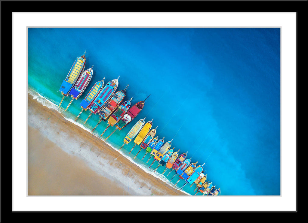 Fotografie von farbigen, nebeneinander liegenden, Fischerbooten am Strand. Fotokunst online kaufen. Wandbild im Rahmen